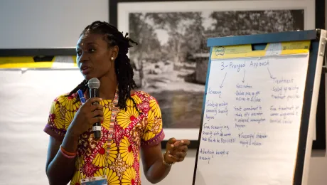 A woman with a microphone standing in front of a flip chart